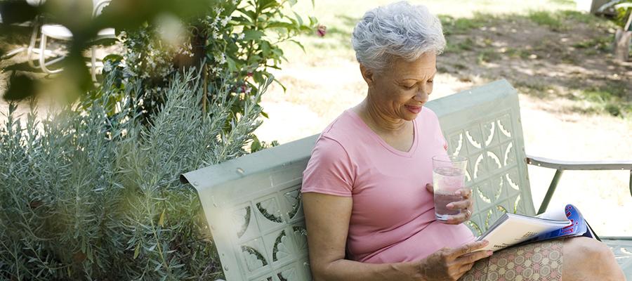 Older woman reading a magazine with a glass of water outside