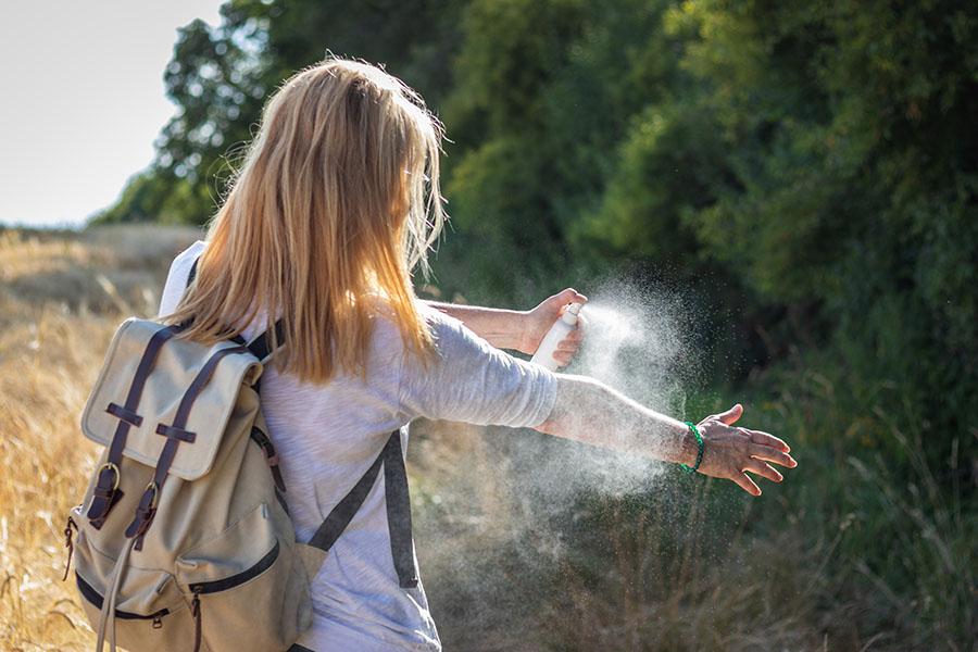 Girl spraying arm with bug spray outside