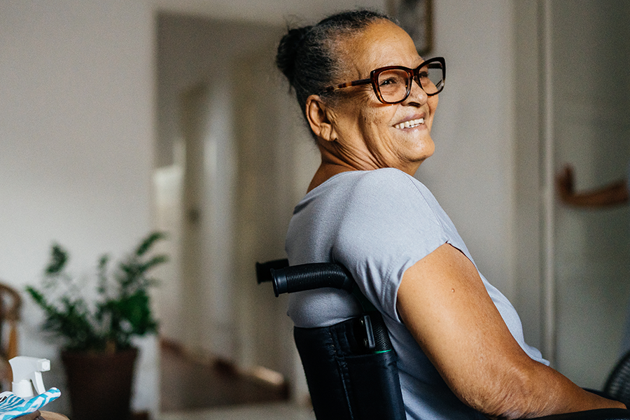 Woman with glasses sitting in wheelchair in a residence looking off camera and smiling